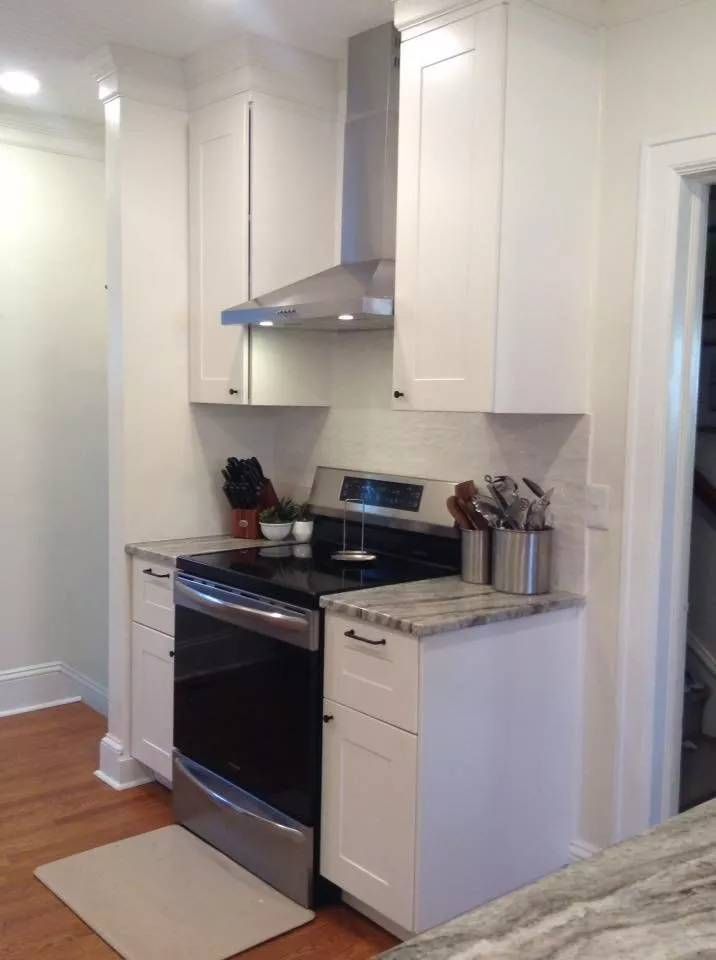 Compact white kitchen with stainless steel stove, hood, and cabinets against a tiled backsplash.