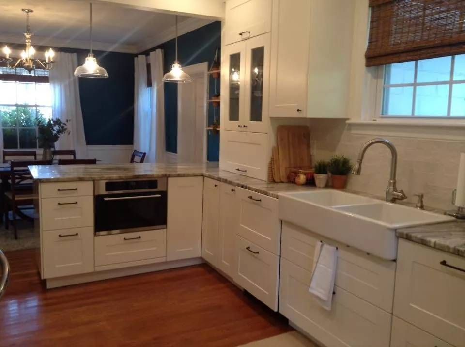 Bright white modern kitchen with farmhouse sink, stainless oven, pendant lights, and hardwood floor.