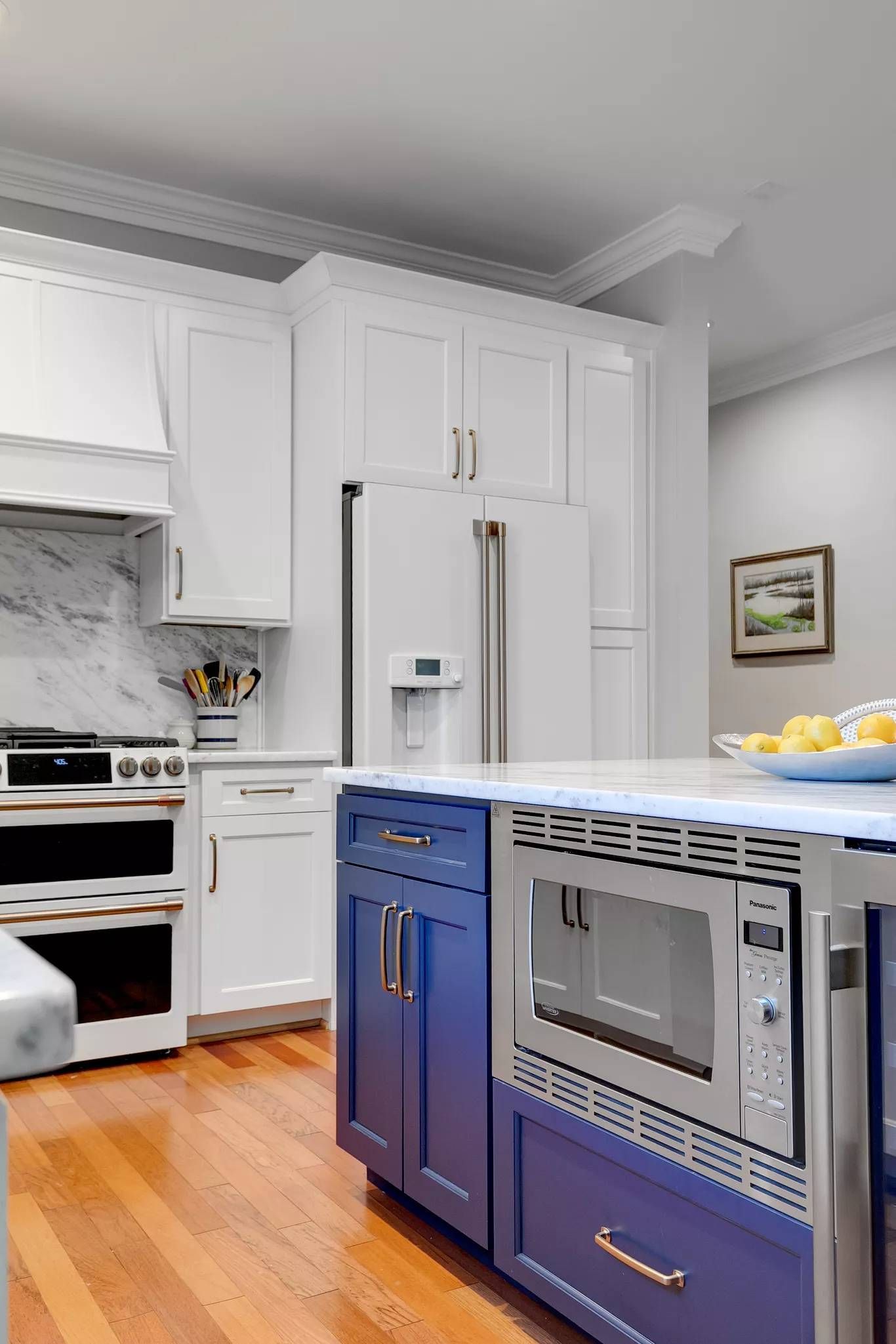 Bright kitchen with white cabinets, blue island, stainless appliances, and wooden floor