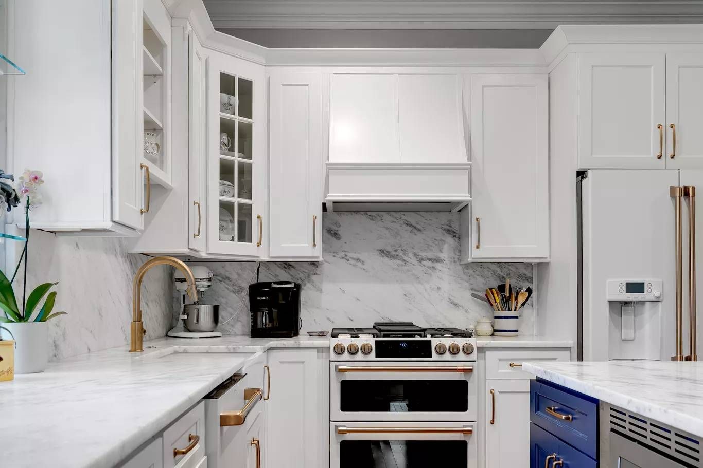 Bright white kitchen with marble counters, stainless oven, glass cabinets, and a refrigerator.