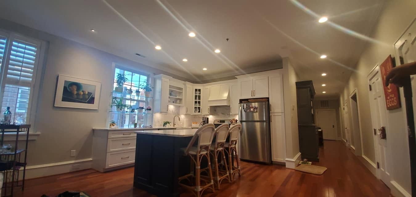 Open kitchen and living room with island seating, hardwood floors, white walls, and stainless steel refrigerator.
