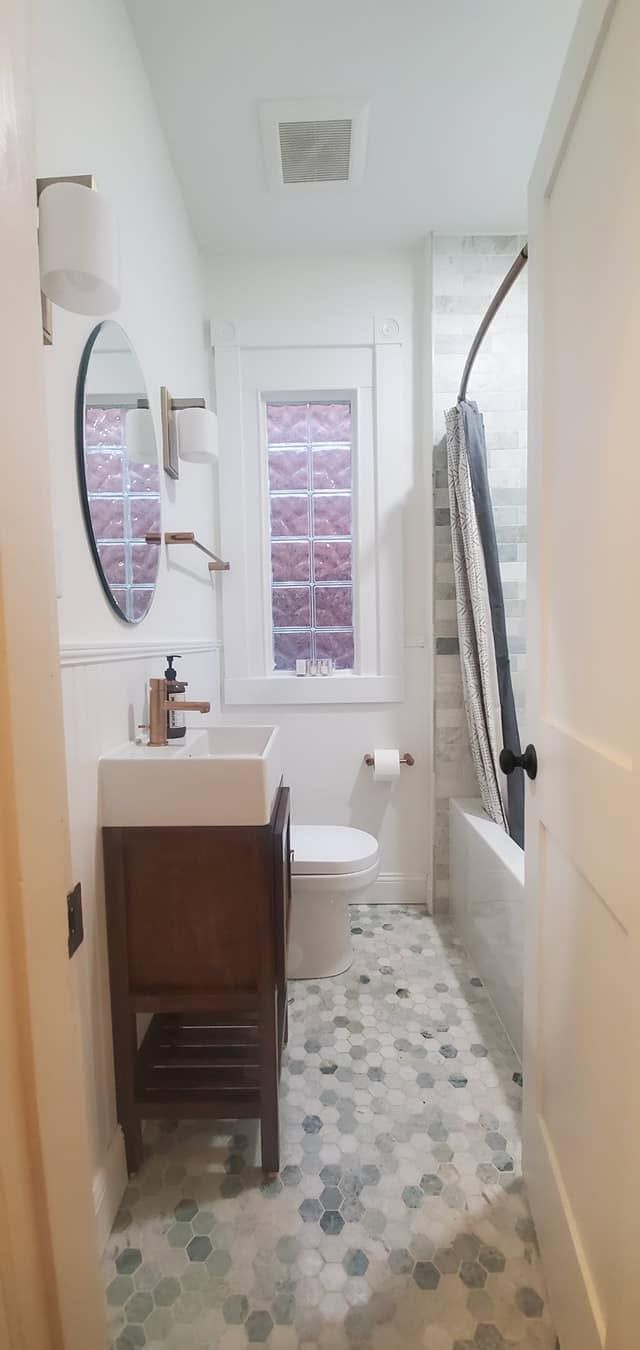 Narrow bathroom with patterned floor, vanity, toilet, window, and a shower curtain.