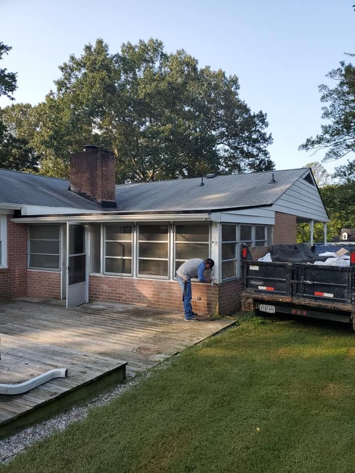 Worker bending beside black truck outside brick house with screened porch and grassy yard