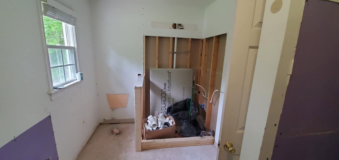 Partially demolished room with exposed studs, debris on the floor, and a window on the left.