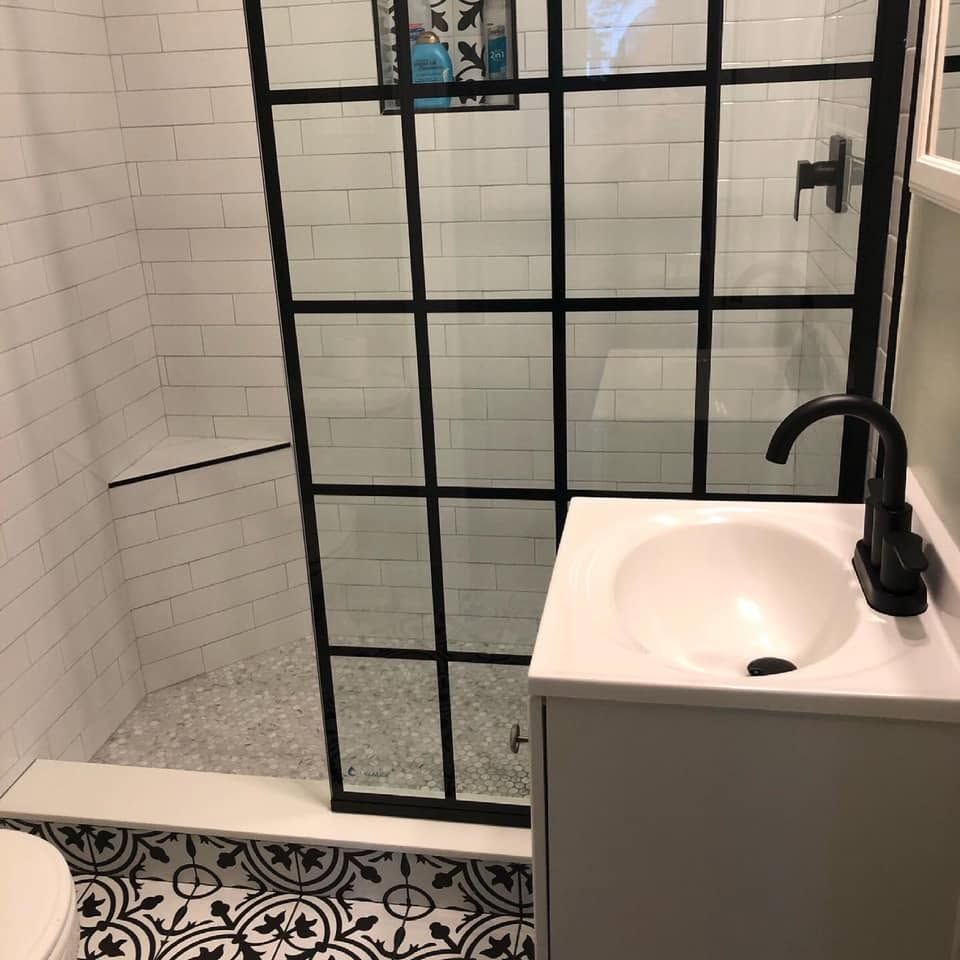 Modern black-and-white bathroom with glass shower, patterned tile floor, and white sink vanity