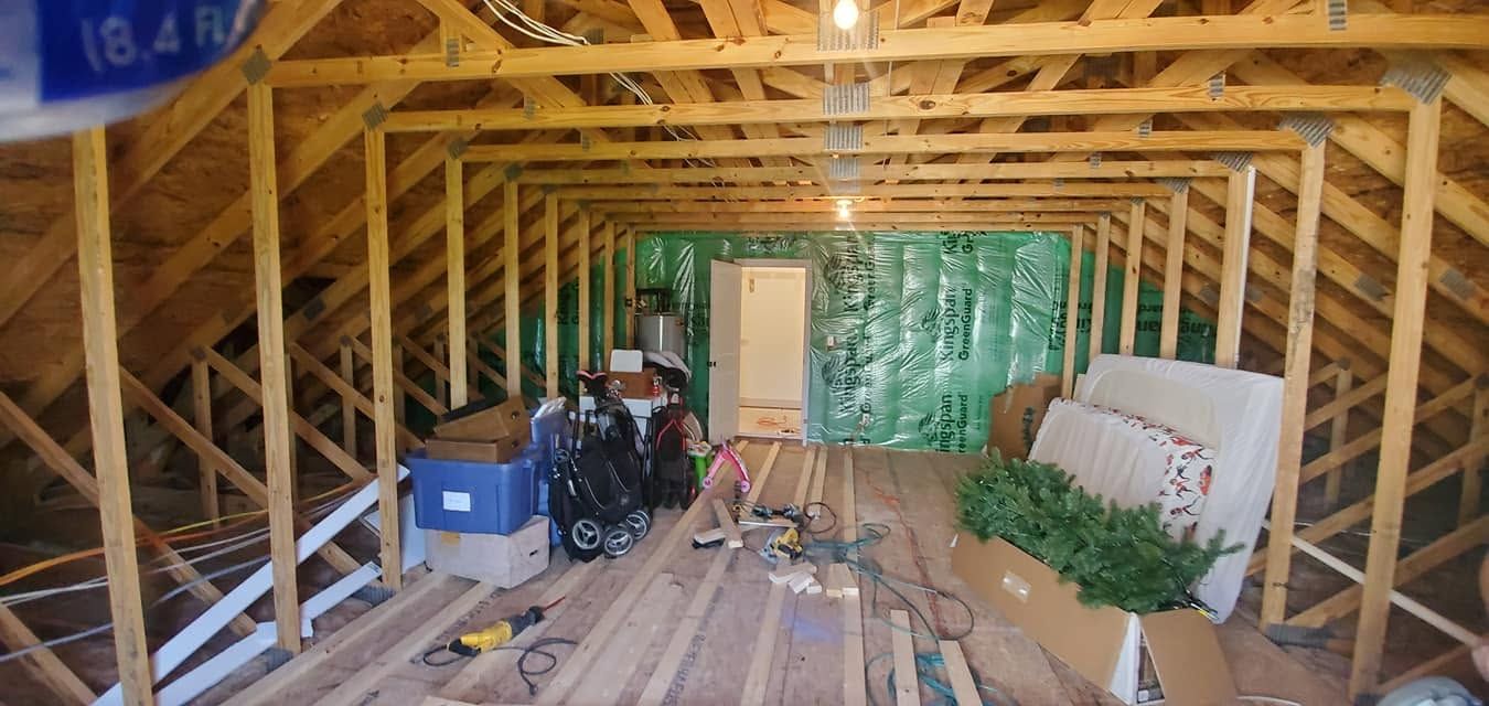 Attic under construction with exposed wooden beams, tools, boards, and stacked materials along the floor and walls