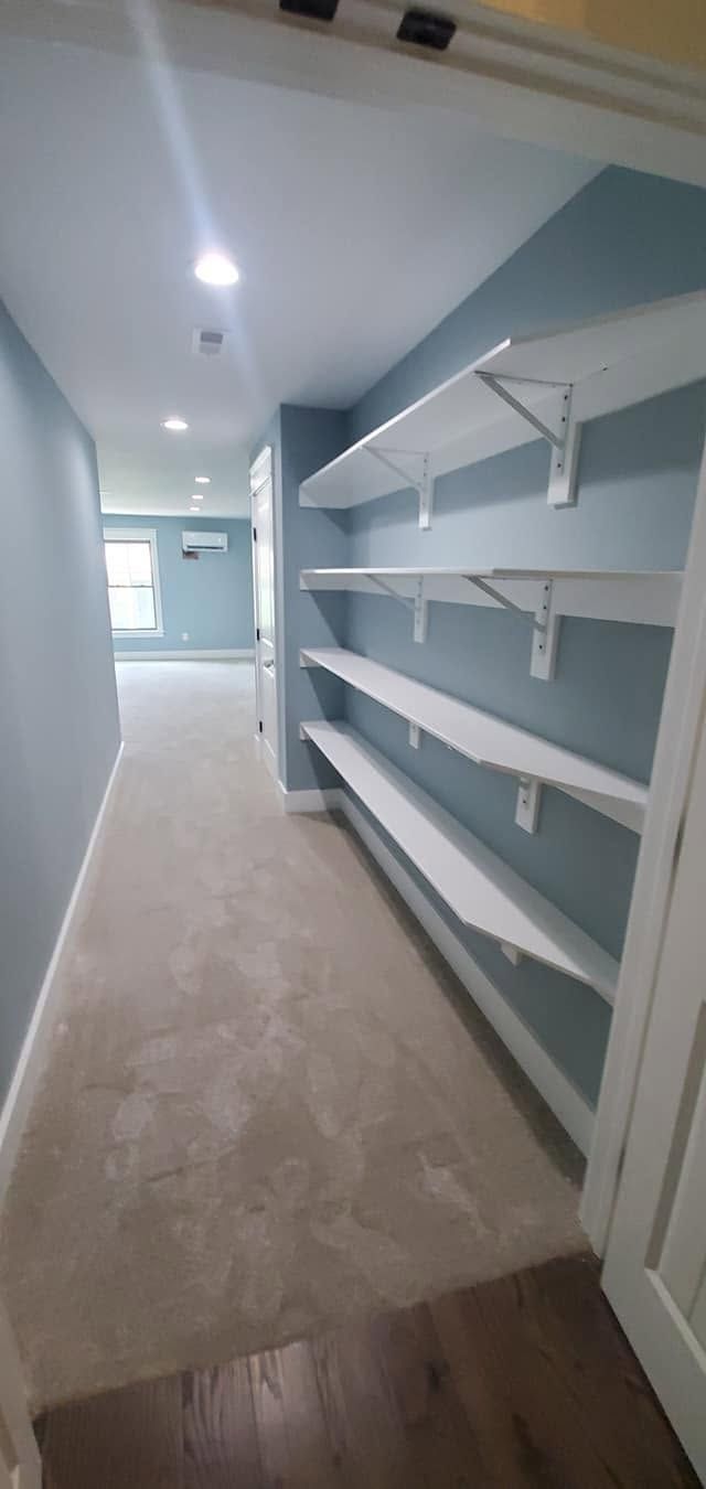 Narrow walk-in closet with white shelves, gray walls, and beige carpet under recessed ceiling lights
