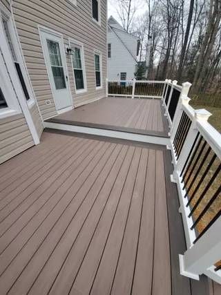 Back deck with gray composite flooring and white railings beside a house, overlooking trees