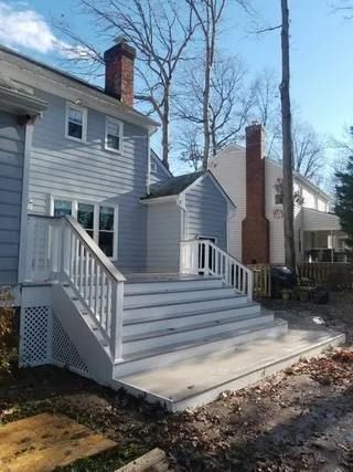 Front steps with white railings leading to a gray house, with a brick chimney and bare trees nearby