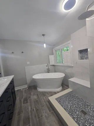 Modern white bathroom with freestanding tub, tiled shower, gray flooring, and window light