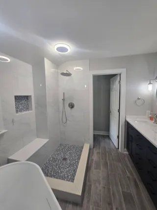 Modern bathroom with walk-in shower, soaking tub, and dark vanity on gray tile flooring