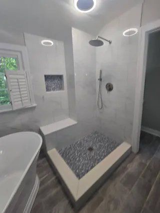 Modern bathroom with walk-in shower, white tub, gray tile floor, and circular ceiling lights