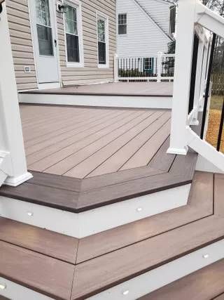 Tiered tan wooden porch deck with white railing and house exterior in the background