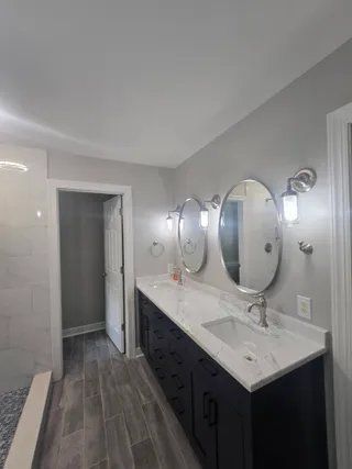 Modern bathroom with double oval mirrors, white marble countertop, and dark vanity cabinets
