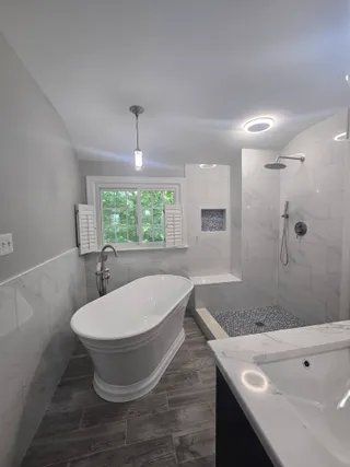 Modern bathroom with freestanding tub, glass shower, vanity sink, and window under soft ceiling lights