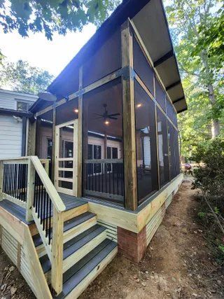 Screened porch with stairs and railing on a raised cabin-style home in a wooded area