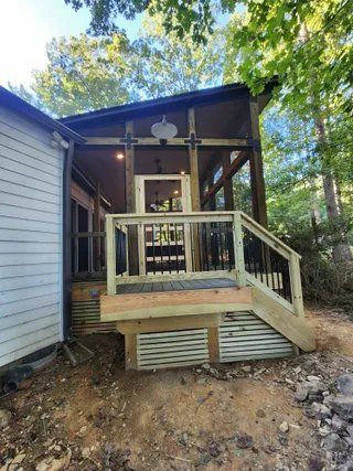Wooden front porch with steps and railing attached to a house, set in a wooded yard.