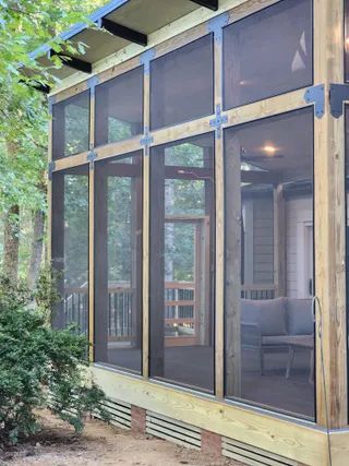 Screened porch with large windows, wood framing, and a sofa inside beside greenery.