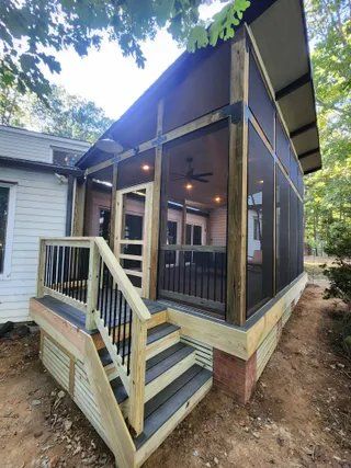 Covered front porch with stairs and railing on a house, featuring screened walls and a sloped roof.