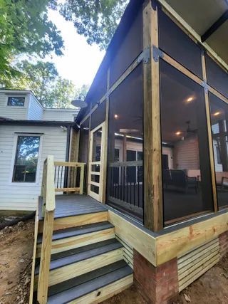 Covered wooden deck with black mesh screens beside a house, reached by stairs and a small ramp.