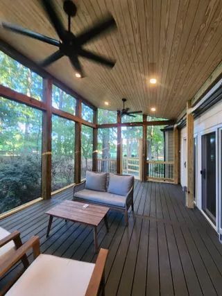 Screened porch with ceiling fans, wood decking, and wicker seating overlooking trees