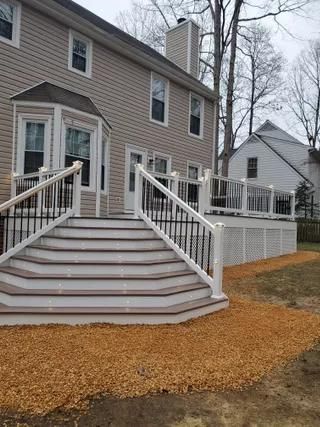 Back steps and ramp leading to a brick house with white railings and winter trees nearby