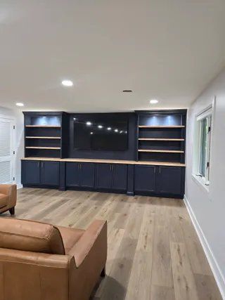 Living room with built-in media wall, dark cabinets, open shelves, and tan chairs on wood floors