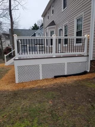 Back deck with white railing and lattice skirting on a beige house, viewed from the yard