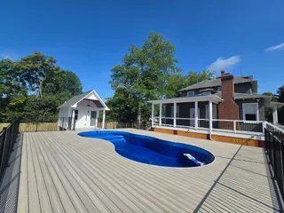 Backyard deck with blue pool and white house under a clear sky