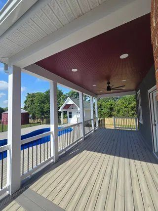 Covered porch with white railings, gray flooring, red ceiling, and ceiling fan overlooking a street and house.
