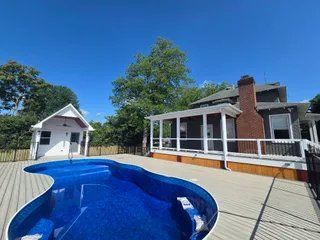 Backyard pool beside a white house and brick chimney under a clear blue sky