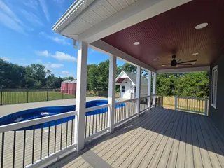 Covered porch overlooking an above-ground pool and fenced backyard with blue sky.