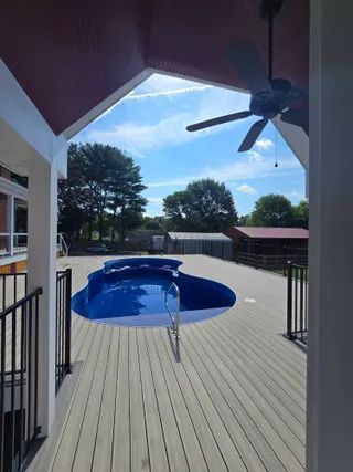 Backyard deck with a small blue pool, railing, and ceiling fan under a covered patio