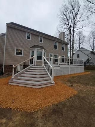 Front of a gray house with wide front steps, white railings, and a fenced patio on a cloudy day