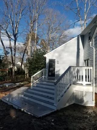 White house exterior with front porch steps and railing, surrounded by leafless trees under a blue sky
