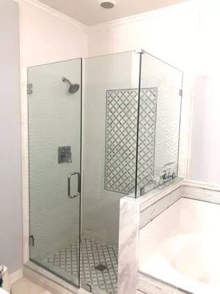 Corner glass shower enclosure beside a white bathtub in a bright bathroom