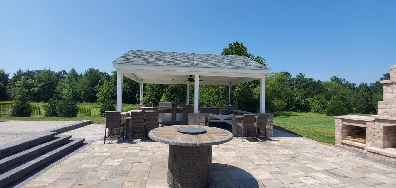 Outdoor stone patio with pergola, circular fire pit, and seating overlooking a green lawn