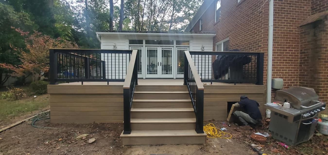 Backyard deck with stairs leading to white French doors and black railings; man kneels near grill on the right.
