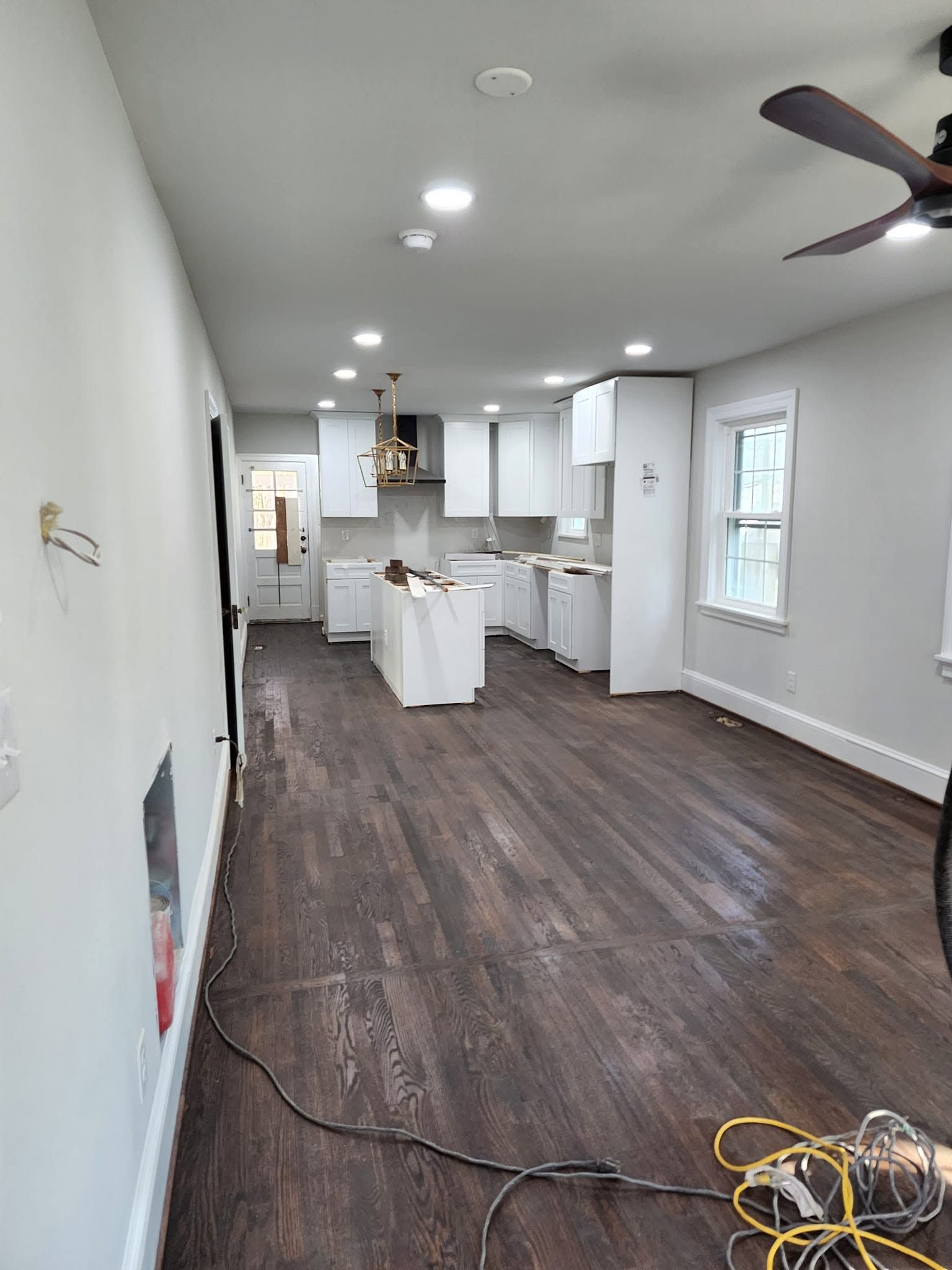 Empty modern kitchen with dark wood floors, white cabinets, island, ceiling lights, and a ceiling fan.