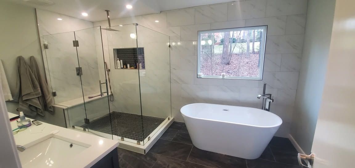 Modern bathroom with glass shower, freestanding tub, and window overlooking trees