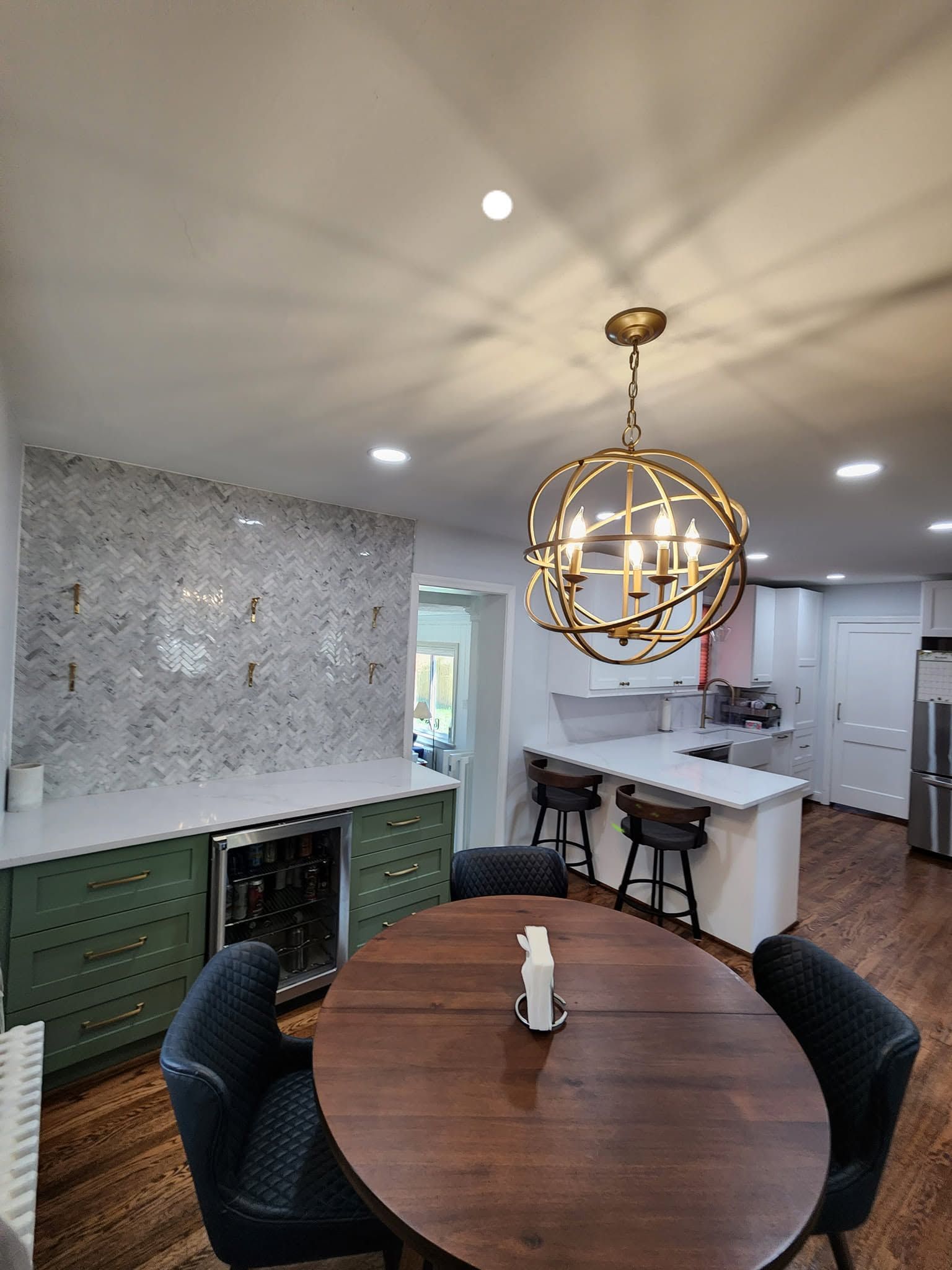 Modern kitchen and dining area with round wood table, black chairs, and gold globe chandelier