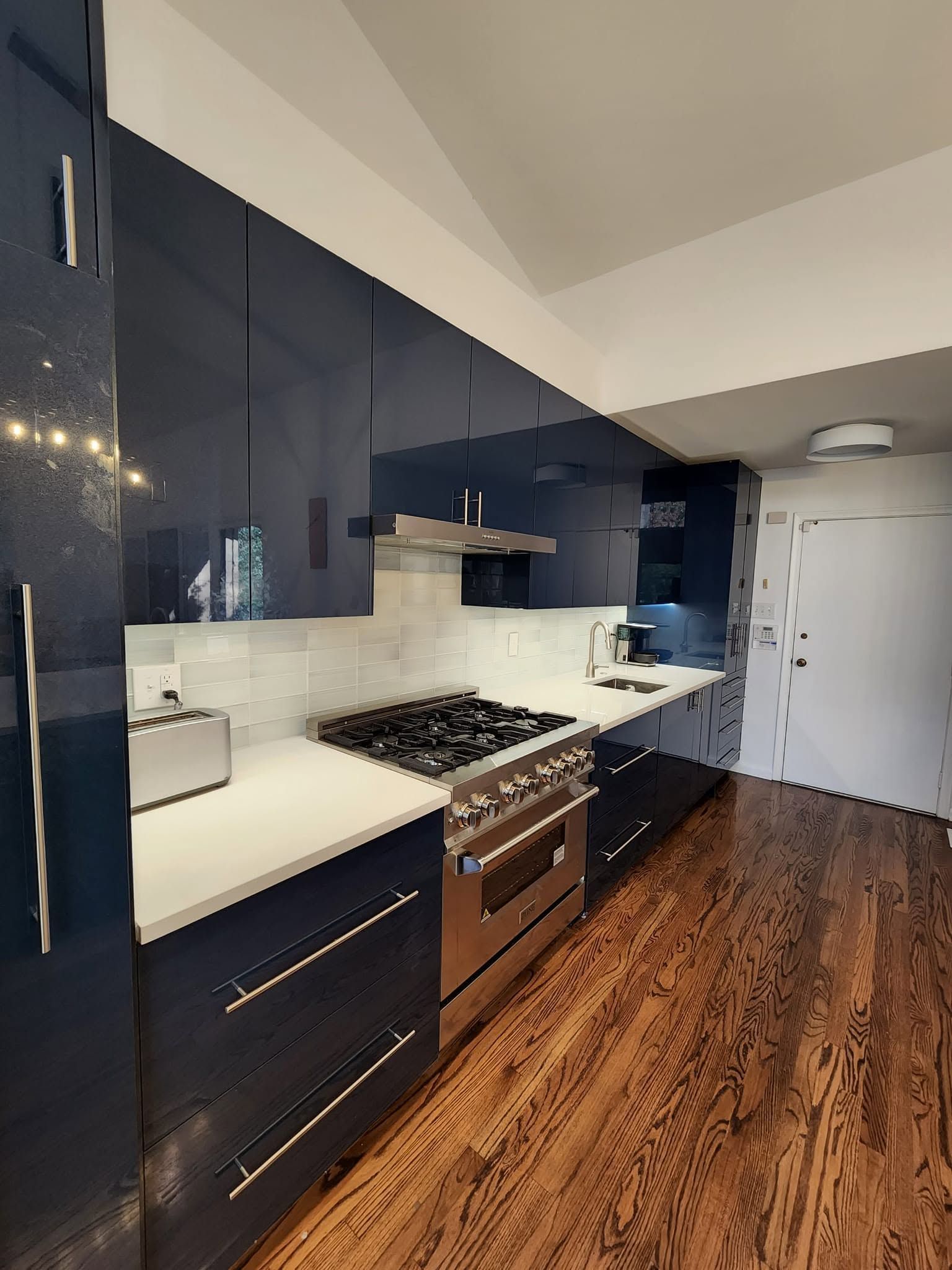 Modern kitchen with navy cabinets, white countertops, stainless stove, and wood flooring.