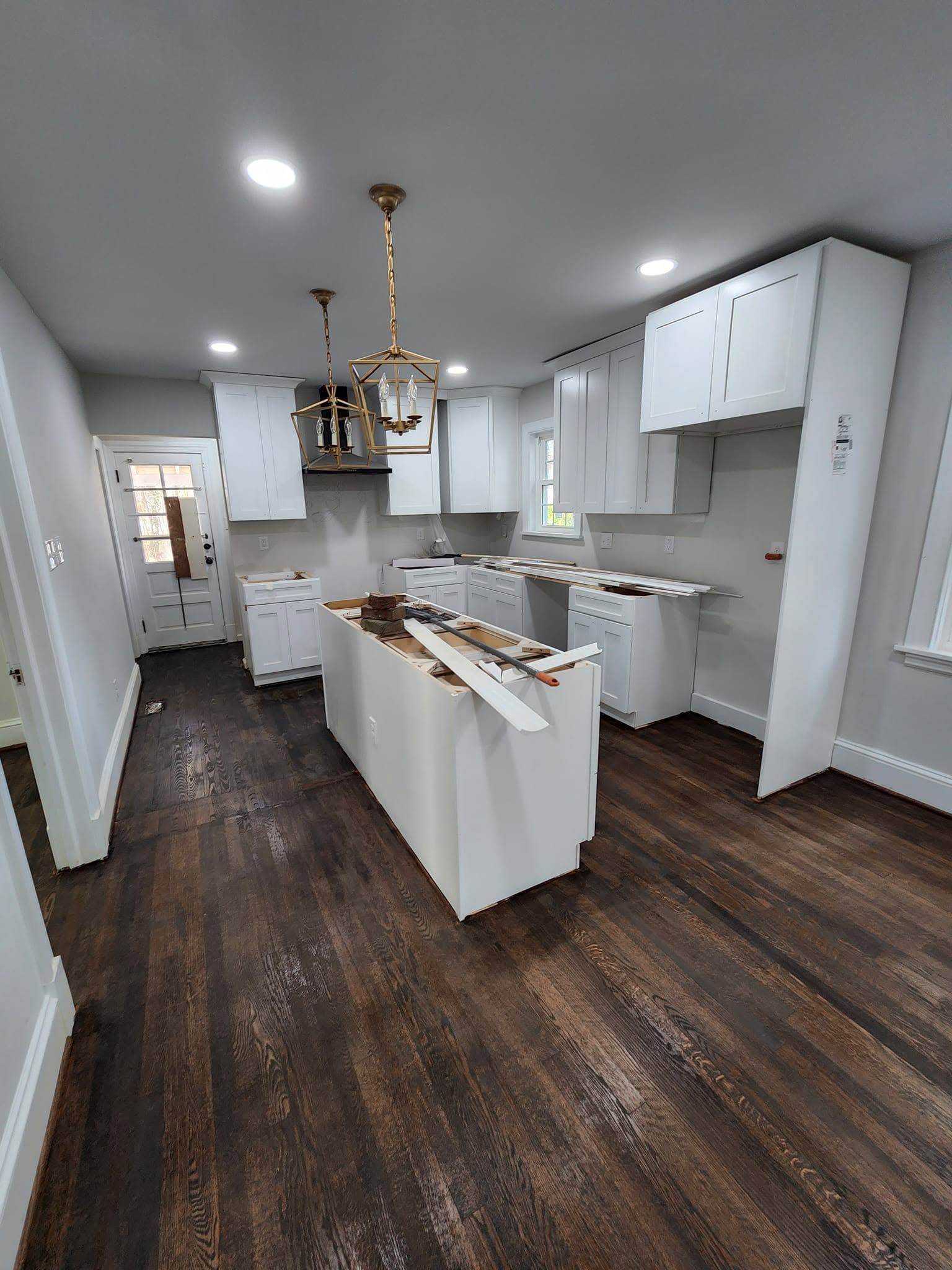 Bright modern kitchen with white cabinets, dark wood floors, and an island under a chandelier.