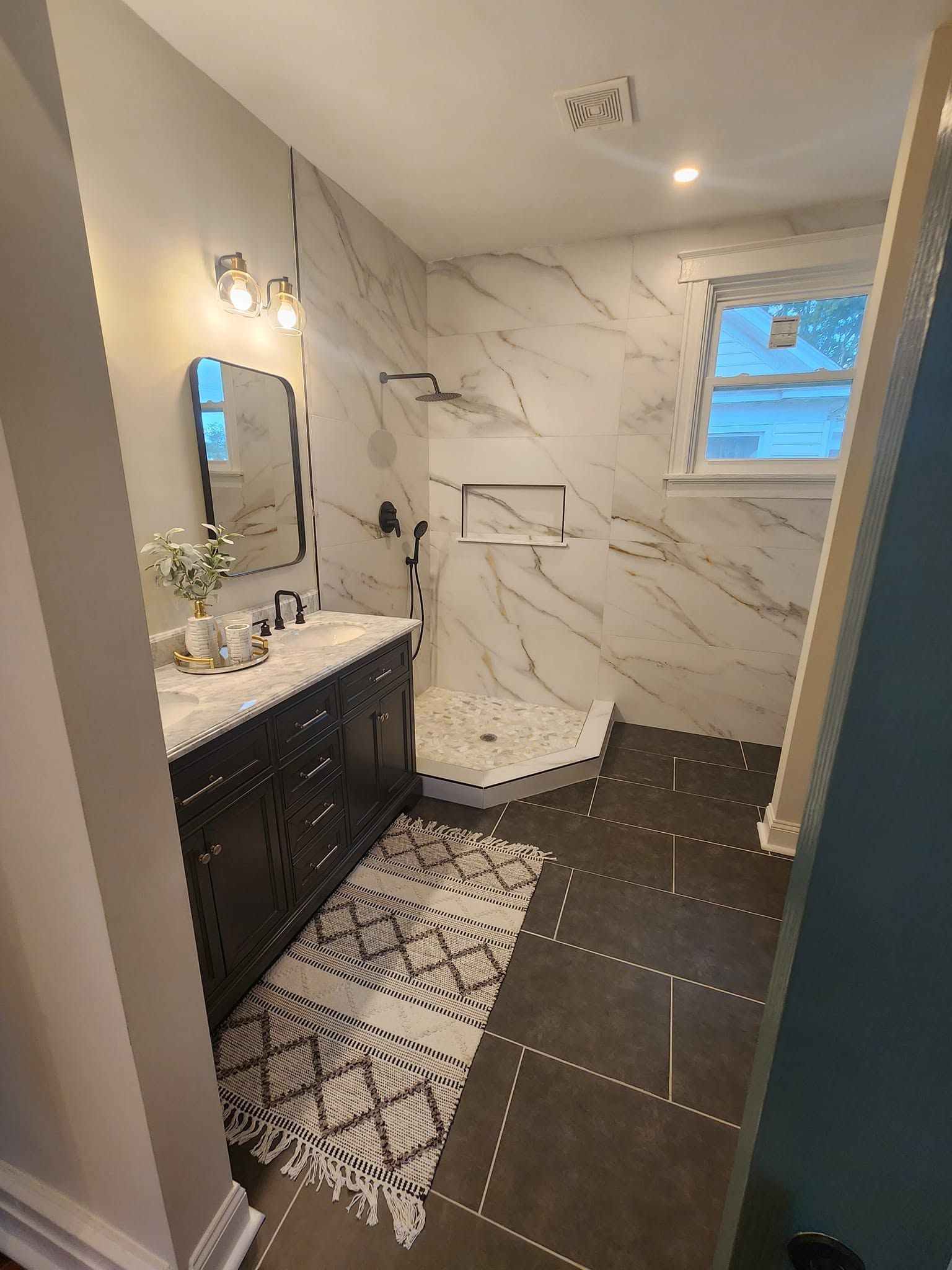 Modern bathroom with marble-look shower, black vanity, white countertop, and dark tile floor