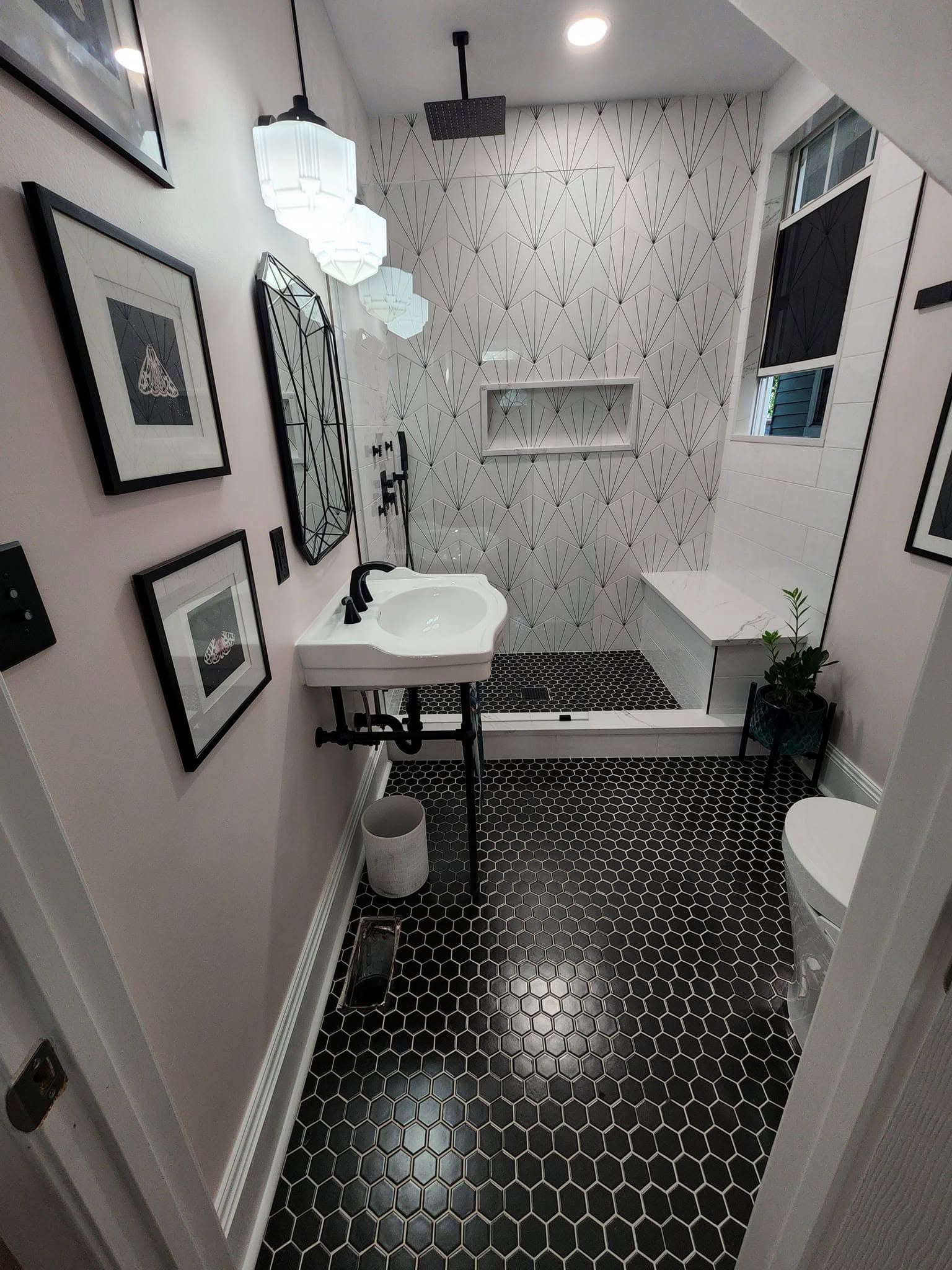 Narrow bathroom with black-and-white tile, white sink, mirror, shower, and framed wall art.