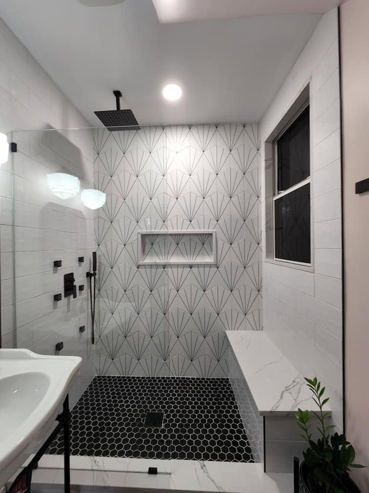 Modern bathroom with shower, bench, patterned tile walls, and sink under bright lighting