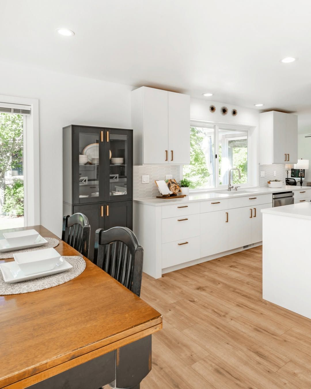 Bright white kitchen with island, wicker bar stools, and large window plants