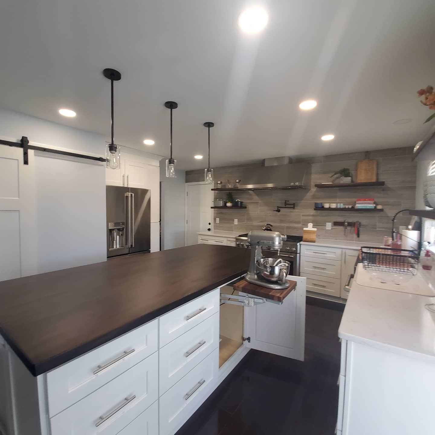 Modern kitchen with white cabinets, dark island countertop, pendant lights, and stainless steel refrigerator