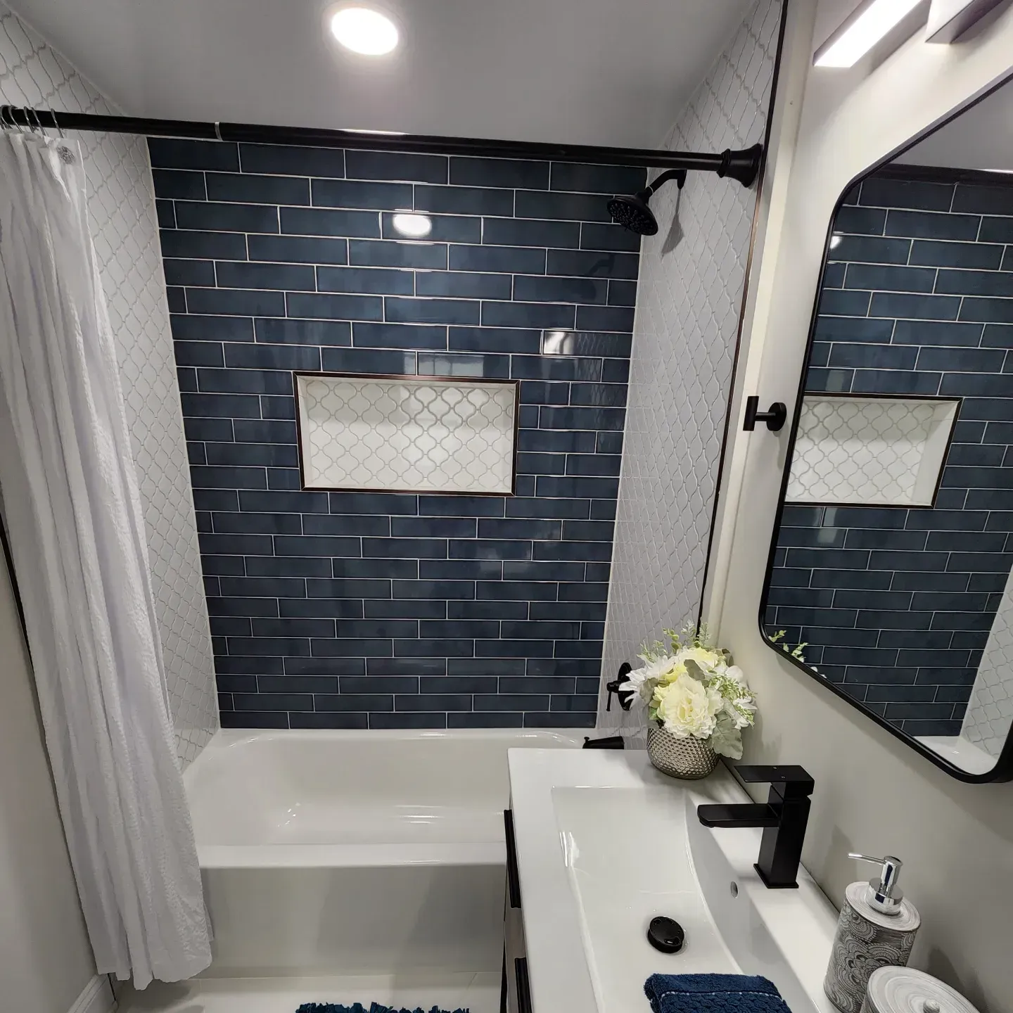 Modern bathroom with black brick tile wall, white tub, vanity sink, and large mirror