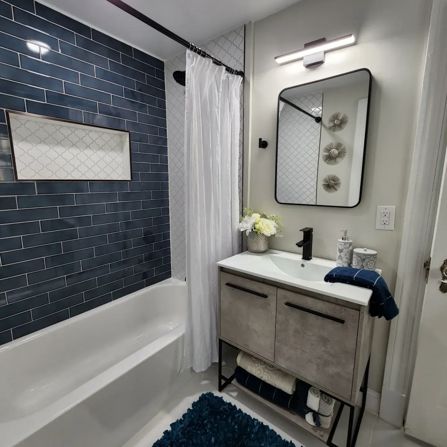 Small bathroom with navy tile accent wall, tub, vanity sink, mirror, and white shower curtain.